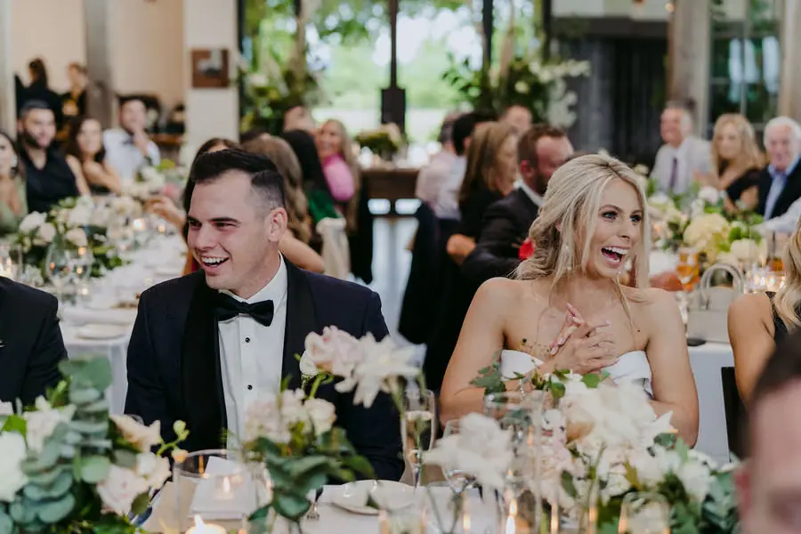 Couple laughs while seated at a floral reception table.