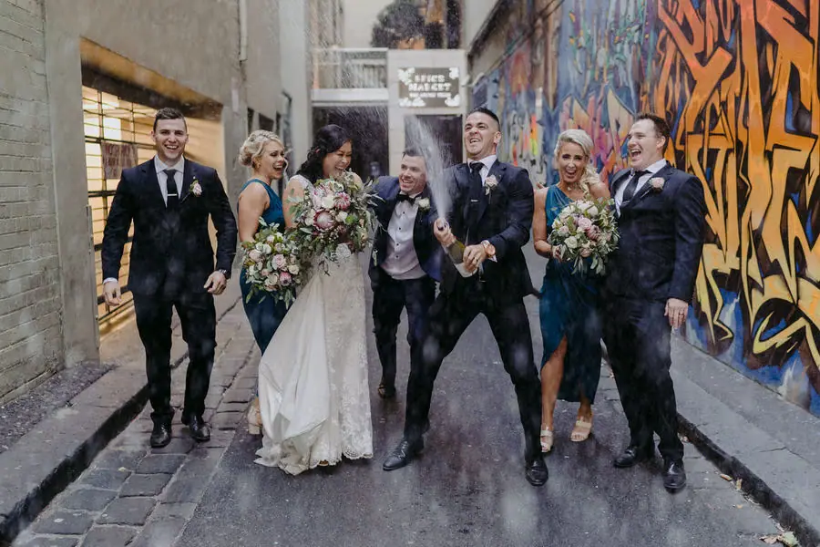 Wedding party walks laughing through a colourful graffiti-covered lane.