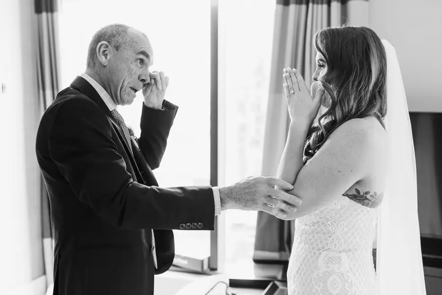 Black and white photograph of the bride and an older man wiping their eyes indoors.