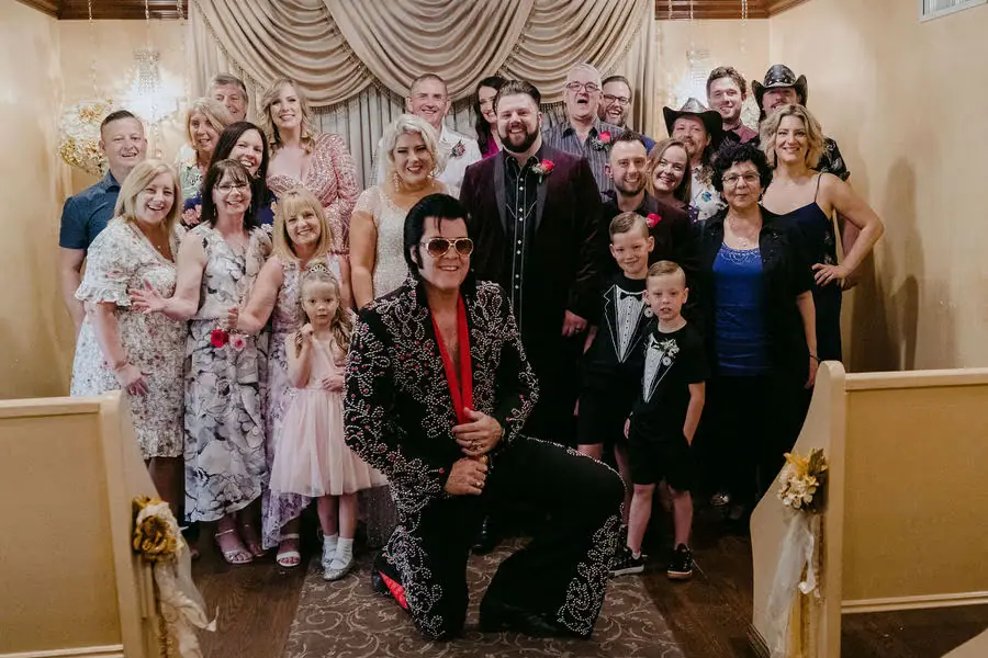Wedding guests pose together with an Elvis-style performer inside a chapel.