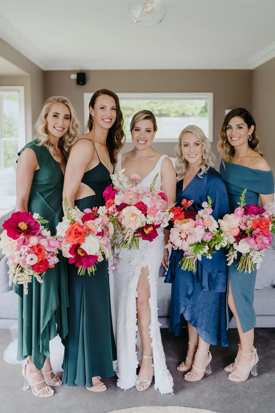 Bride and bridesmaids pose with vivid pink and orange bouquets indoors.