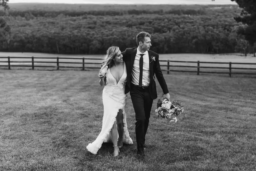 Black and white photograph of the couple walking arm in arm across a field.