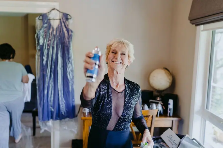 Older woman smiles while holding a small spray bottle toward the camera.