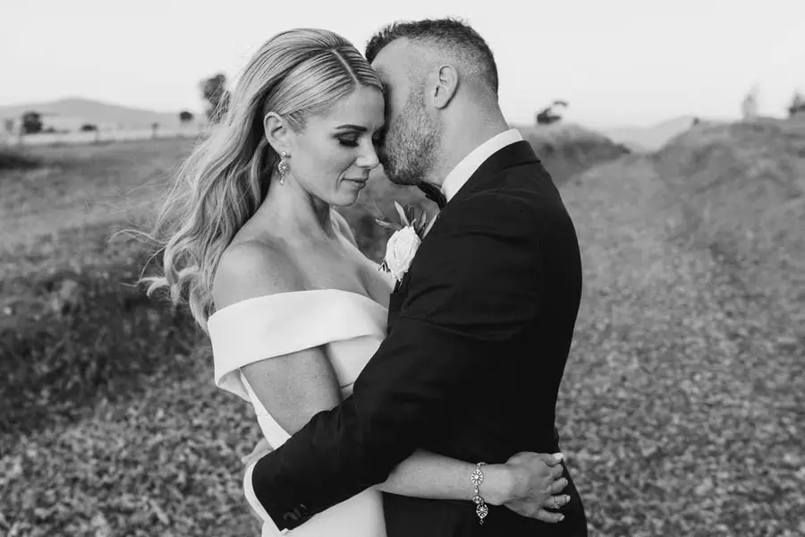 Black and white portrait of the groom kissing the bride's forehead in a field.