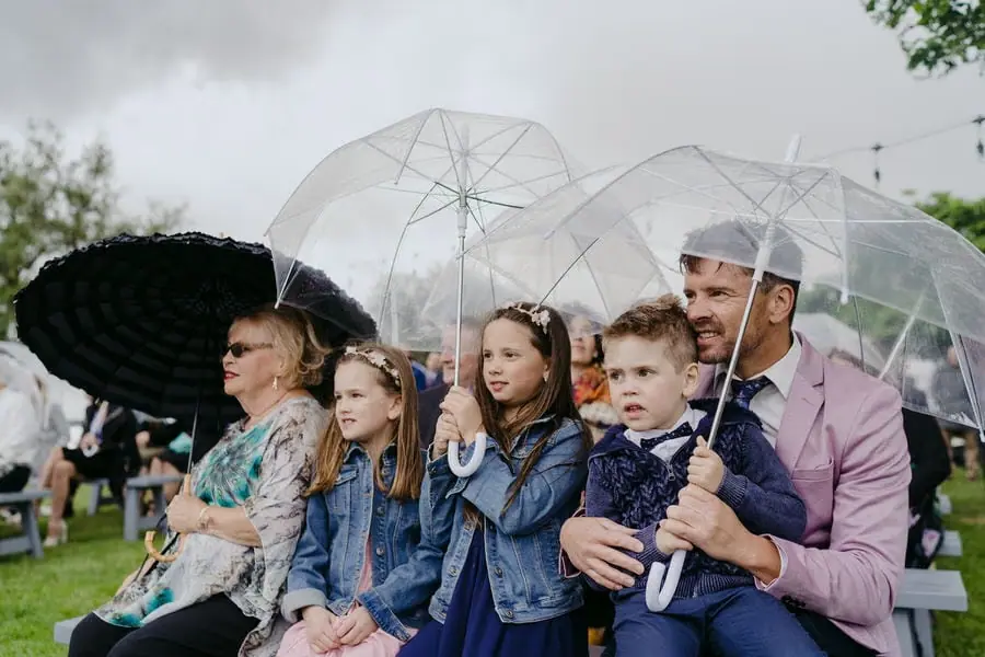 Guests and children shelter beneath clear umbrellas at a rainy ceremony.