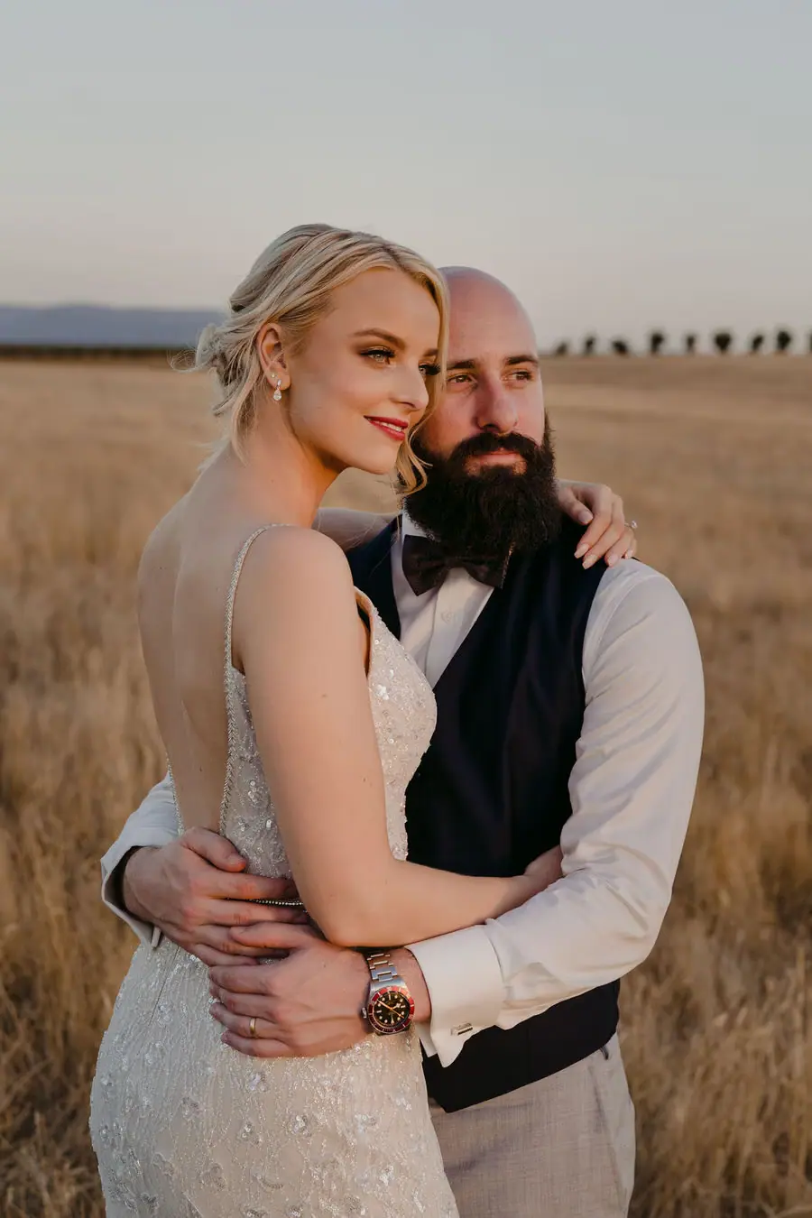 Couple embraces closely together in a dry field at dusk.