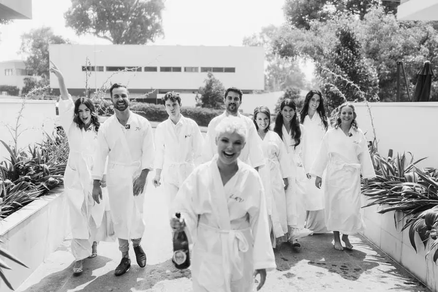 Black and white photograph of women in white robes celebrating with champagne outdoors.