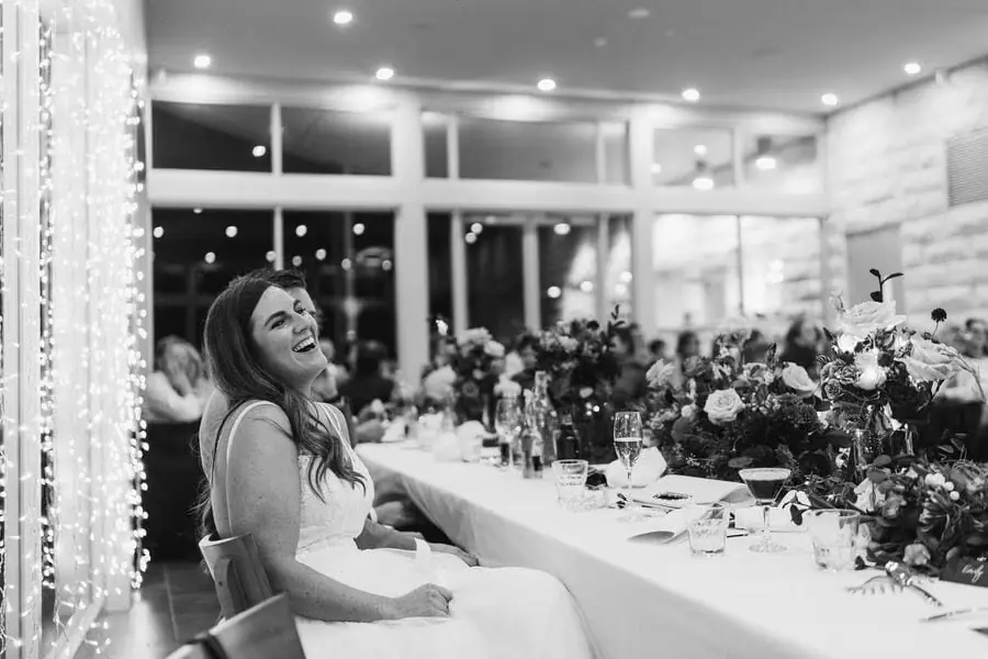 Black and white photograph of the bride laughing at the reception table.