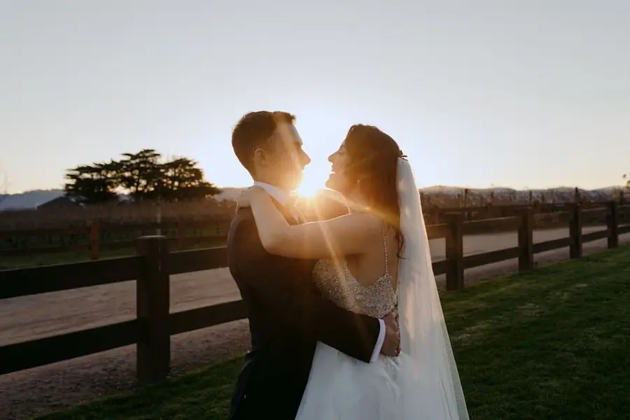 Couple embraces beside a wooden fence with sunset light between them.