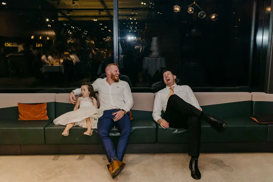 Two men and a child relax on a sofa at the nighttime reception.