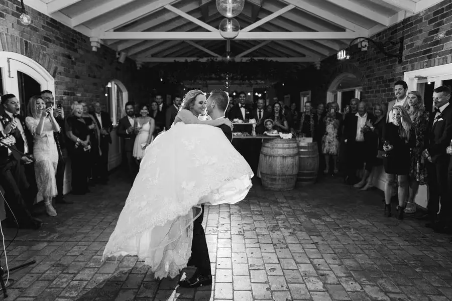 Black and white photograph of the groom lifting the bride on a brick reception floor.