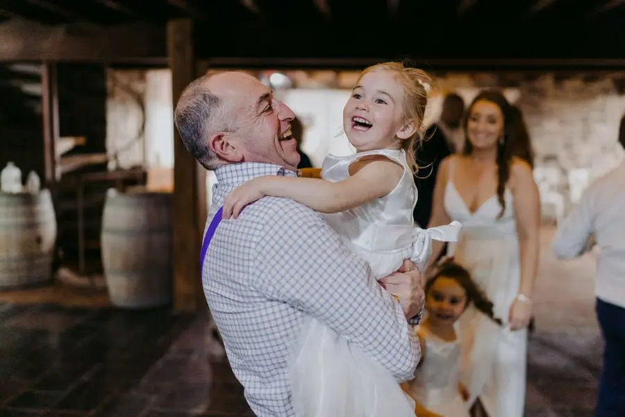 Man holds a laughing small girl with the bride smiling behind them.