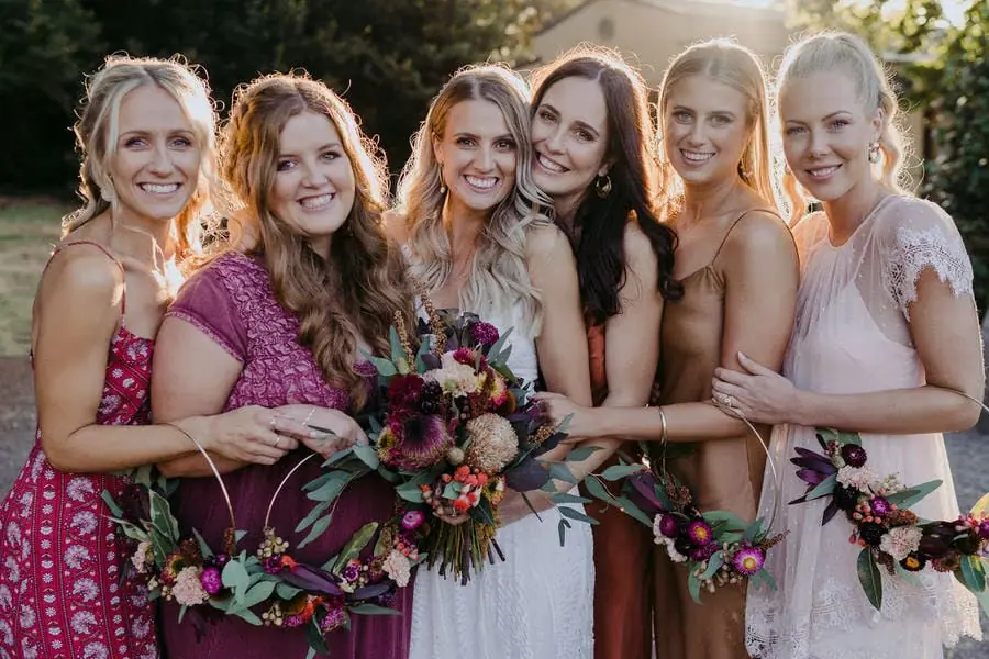 Bride and friends lean together smiling with colourful bouquets.