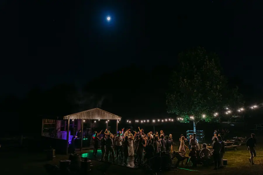 Guests gather beneath outdoor string lights with the moon overhead.