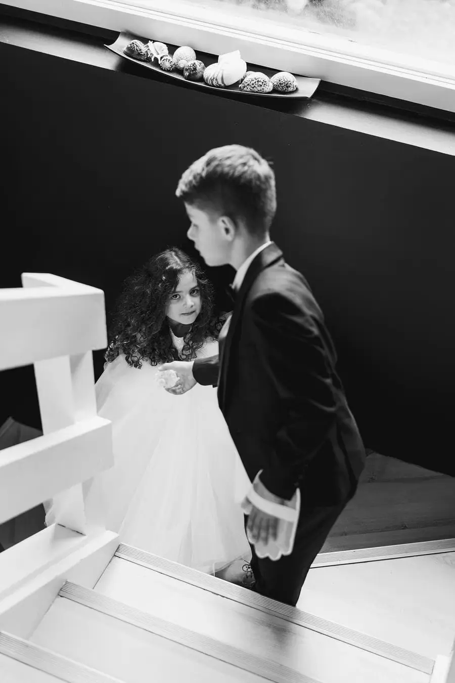 Black and white photograph of a boy and a small girl in wedding clothes on stairs.