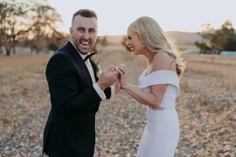 Couple laughs while holding hands in a dry field.