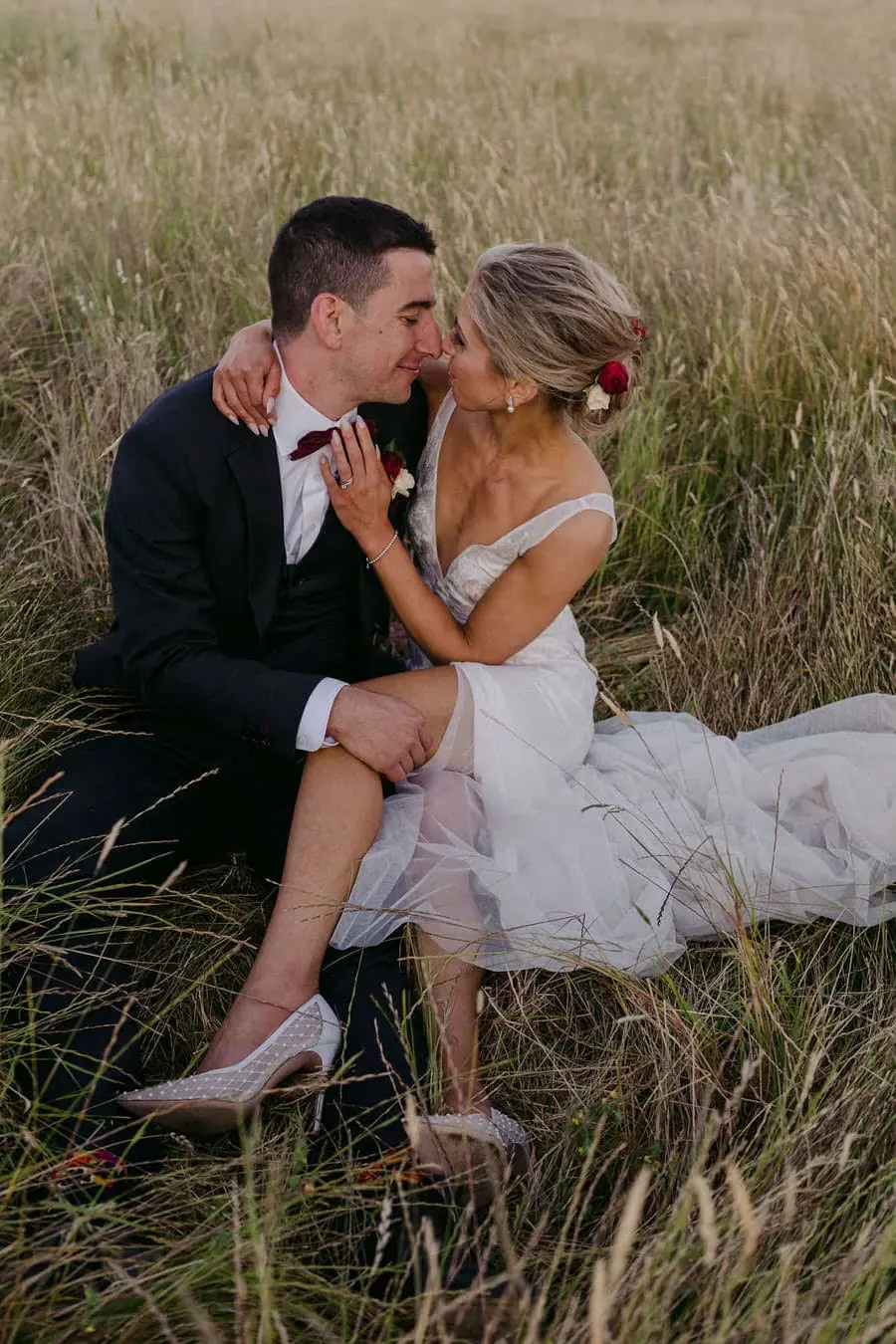 Couple kisses while seated together in long grass.
