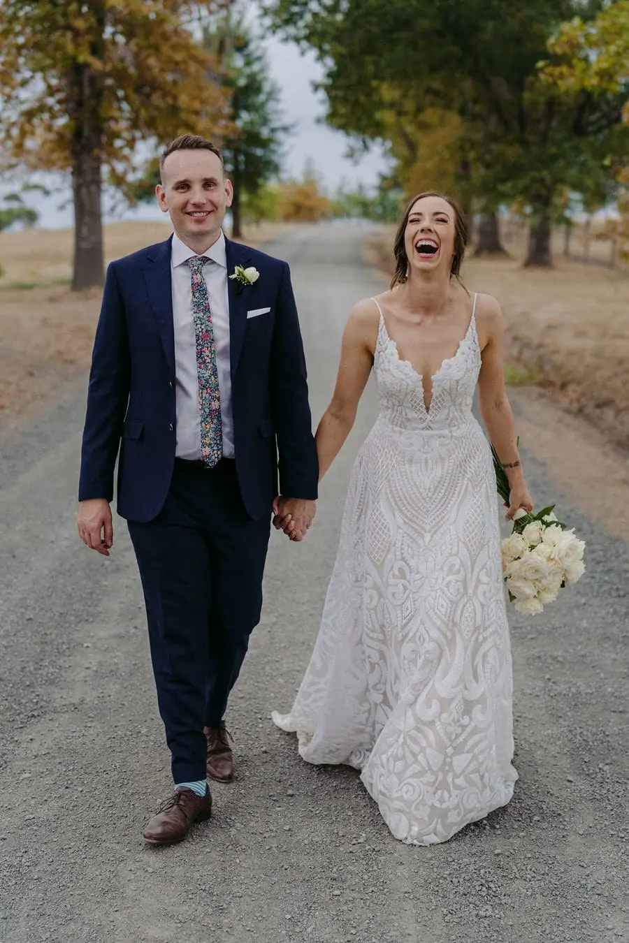 Couple walks hand in hand along a road laughing together.