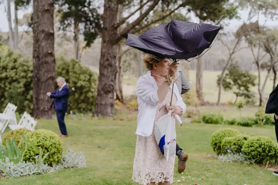 Guest holds an umbrella turned inside out by the wind at an outdoor ceremony.
