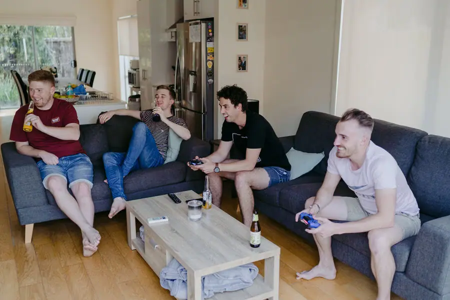 Men relax on sofas with drinks and game controllers indoors.