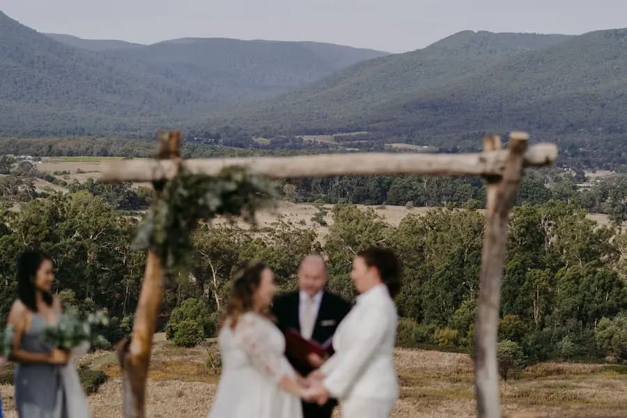 Outdoor ceremony beneath a rustic wooden arch overlooking a valley and mountains.