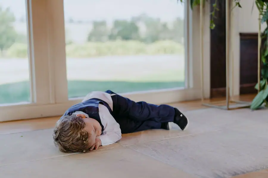 Young boy in wedding clothes lies curled up on the floor beside a window.