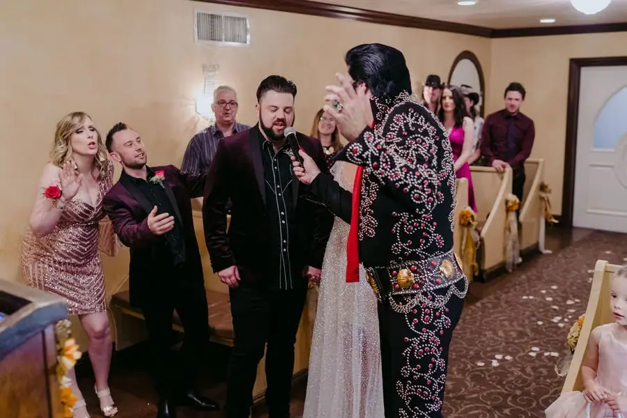 Elvis-style performer sings beside the couple and guests in a chapel.