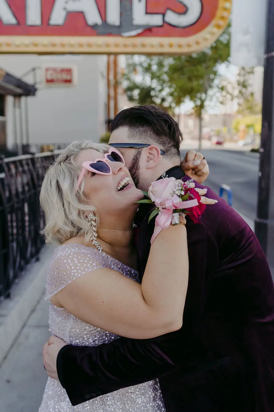 Couple wearing sunglasses embraces and kisses on a city street.
