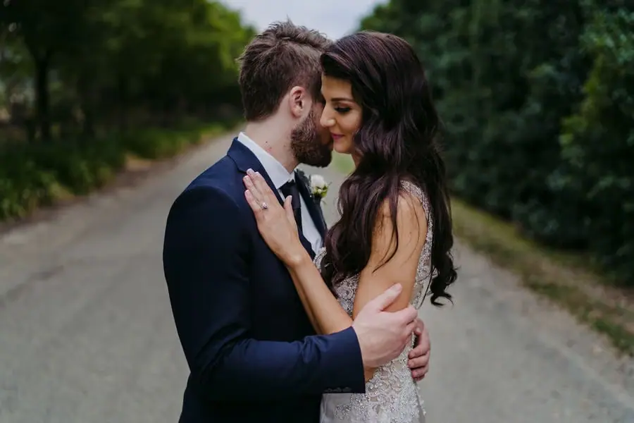 Couple rests their foreheads together on a quiet leafy road.