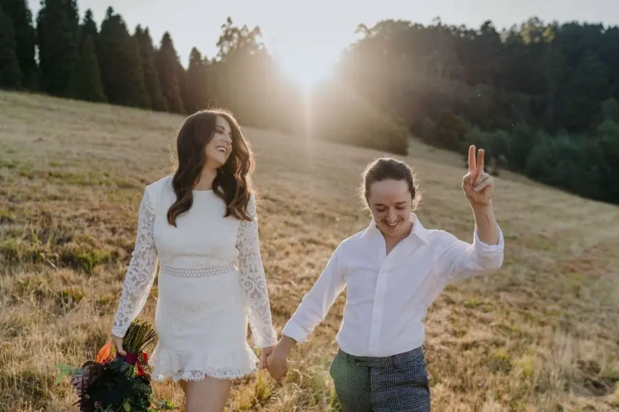 Couple walks hand in hand through a dry field with one raising a peace sign.