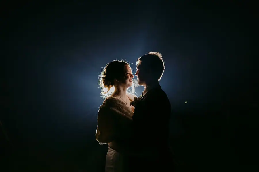 Couple faces each other in a dark portrait with bright backlighting around their profiles.
