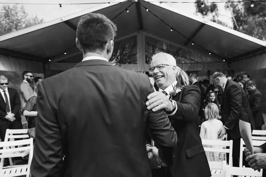 Black and white photograph of an older man greeting the groom among wedding guests.