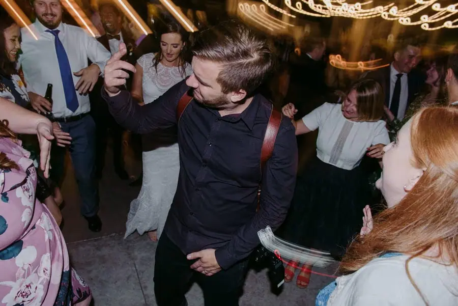 Guest dances with a drink in his hand beneath blurred reception lights.