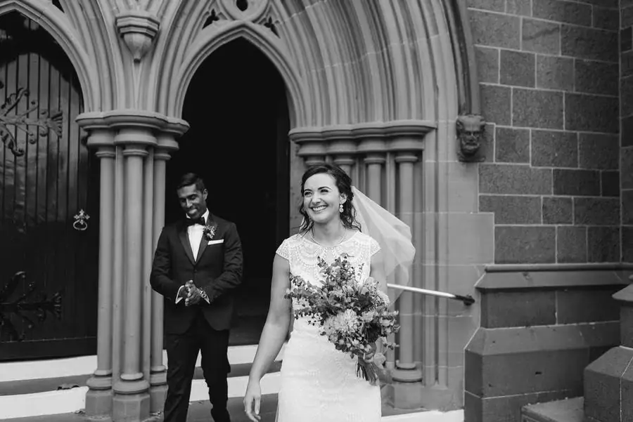 Black and white photograph of the couple leaving a grand stone church doorway.