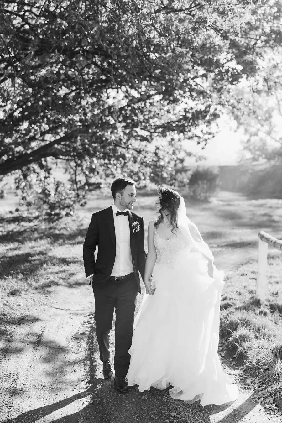 Black and white photograph of the couple walking arm in arm along a sunlit path.