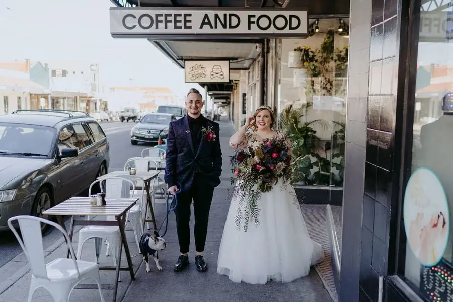 Couple laughs while walking beside a street café with a colourful bouquet.
