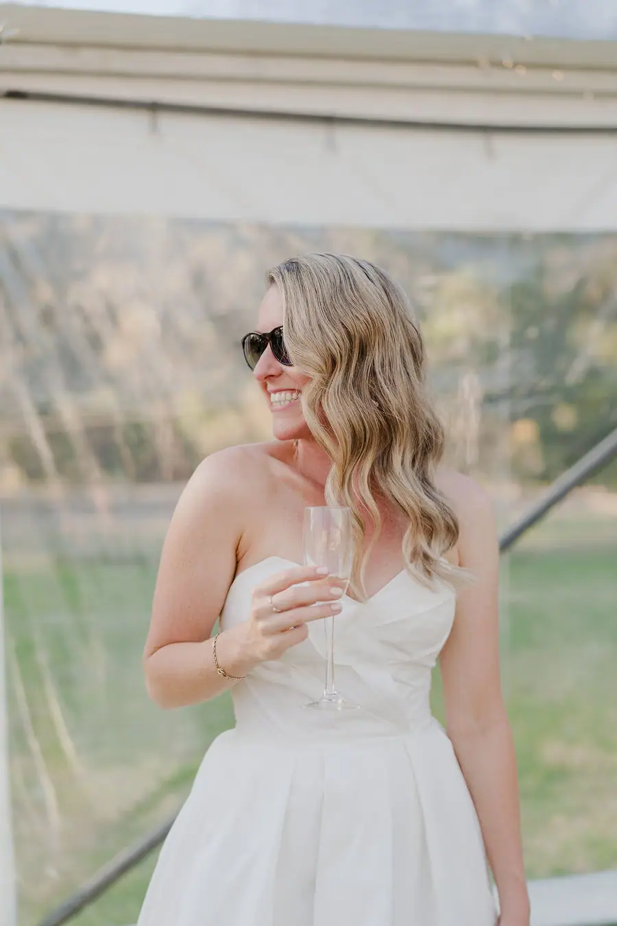 Bride wears sunglasses and holds a drink inside the reception tent.