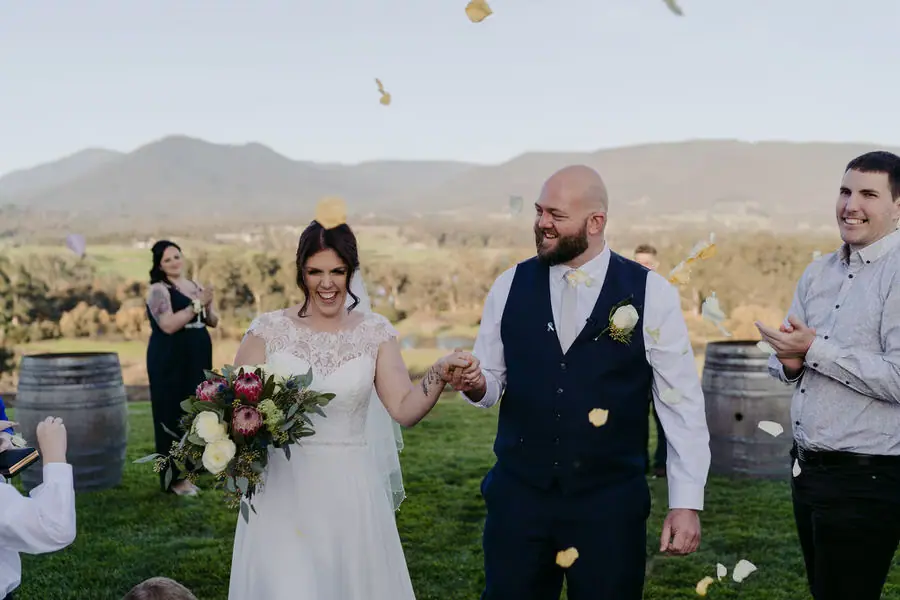 Newlyweds hold hands as guests toss petals at their outdoor ceremony.