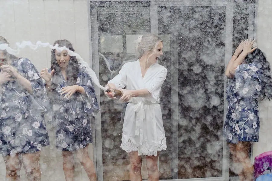 Women in robes laugh and shield their faces from champagne spray.