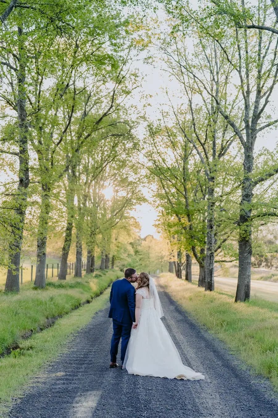 Rear view of the couple walking along a leafy tree-lined road.