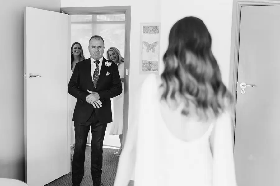 Black and white photograph of an older man seeing the bride from an open doorway.