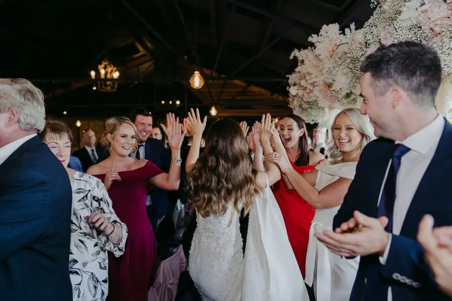 Bride celebrates with guests raising their hands on the reception dance floor.