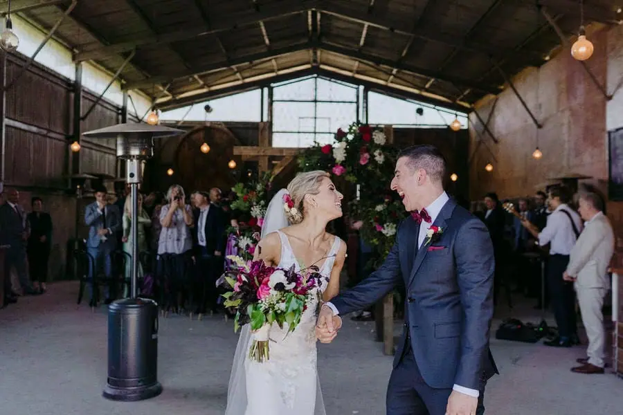 Couple smiles toward each other as they enter a large rustic reception venue.