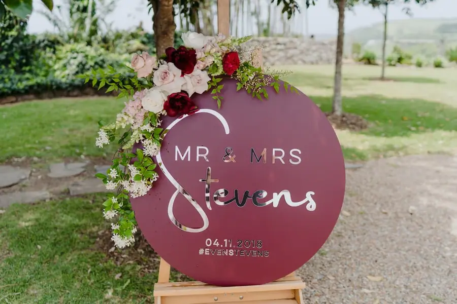 Round burgundy wedding welcome sign decorated with flowers on a wooden easel