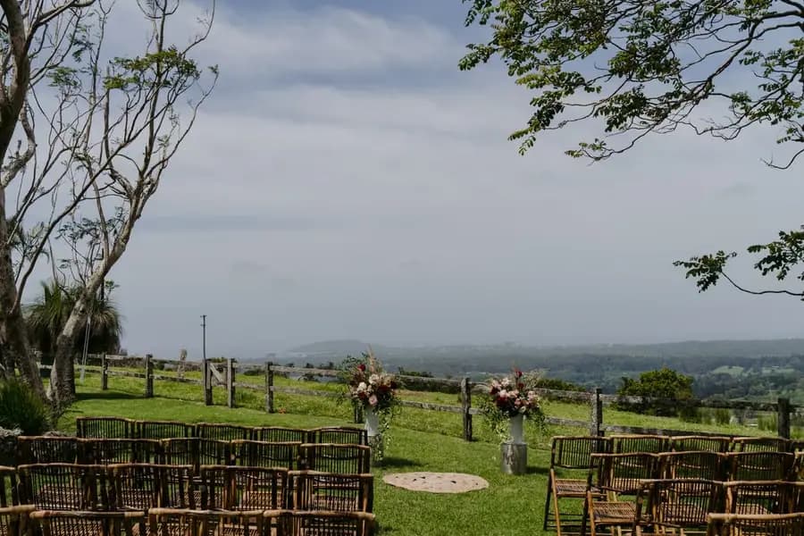 Rows of ceremony chairs facing floral stands and distant green hills