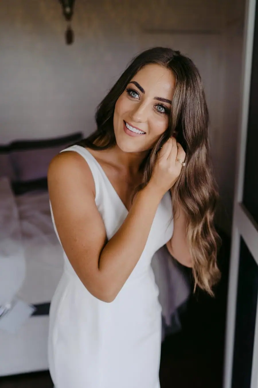 Bride smiling while putting on an earring indoors