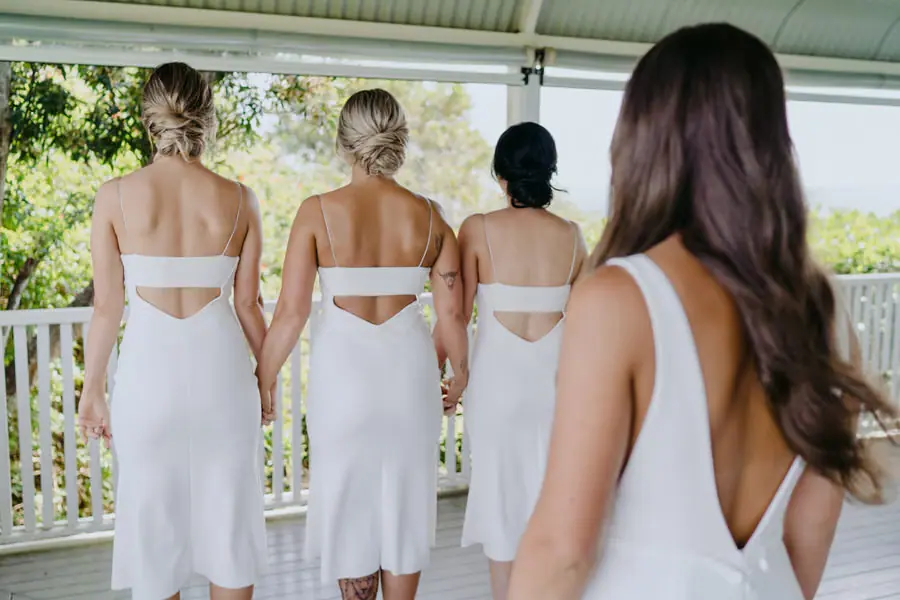 Three bridesmaids in white dresses standing with their backs to the approaching bride