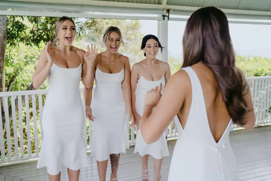 Bridesmaids turning toward the bride with delighted expressions on a veranda