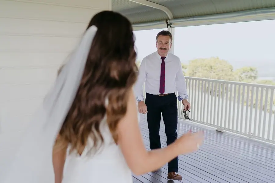 Bride greeting a smiling man in a white shirt and burgundy tie on a veranda