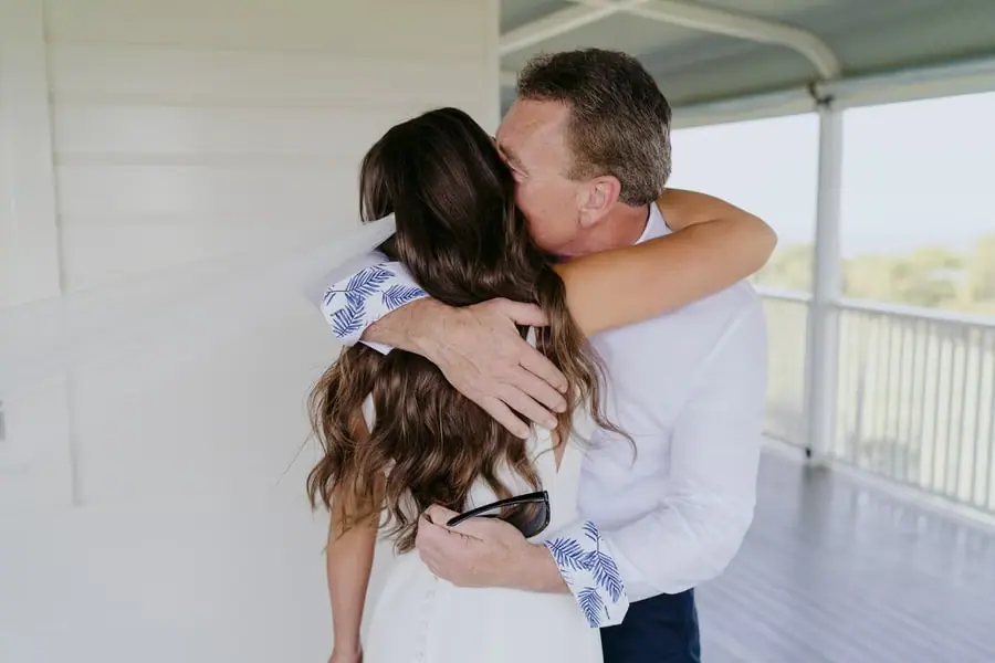 Bride embracing a man in a white shirt on a veranda